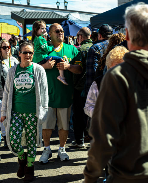 Arvada, Colorado, USA, March 11, 2023, large father dressed in green shirt hold daughter dressed in green shirt in his arms among street crowd Arvada, Colorado, USA, March 11, 2023, large father dressed in green shirt hold daughter dressed in green shirt in his arms among street crowd arcada stock pictures, royalty-free photos & images