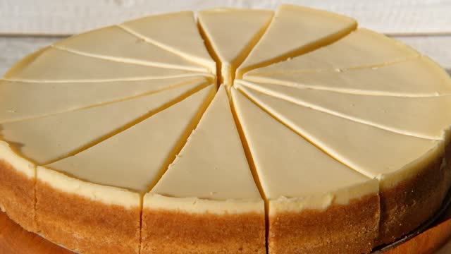 Plain Cheesecake cake close-up spinning on turntable. Cakes in a coffee shop. Many slices of classical New york cheesecake. Whole cheesecake with slice cut out is rotating. Top View. Cheese cream tart