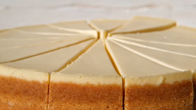 Plain Cheesecake cake close-up spinning on turntable. Cakes in a coffee shop. Many slices of classical New york cheesecake. Whole cheesecake with slice cut out is rotating. Top View. Cheese cream tart