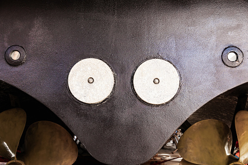 The back of a large motor yacht, standing on wooden blocks in a dry dock. Two propellers and zinc protective inserts.