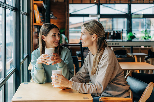 Two women sitting in a coffee house talking and drinking coffee.