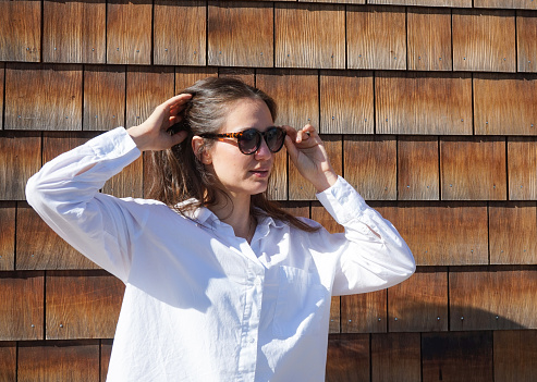 Woman wearing sunglasses while standing against wooden wall