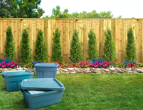 Group of blue plastic storage totes in a backyard with a fence