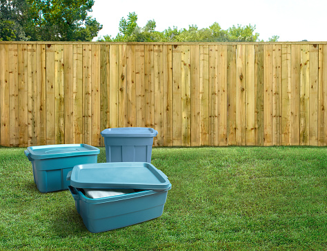 Group of blue plastic storage totes in a backyard with a fence