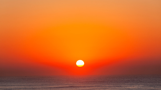 Ocean horizon with sun rising over the ocean water surface  in clear sky with blend mix of red orange colors a scenic moment of nature.