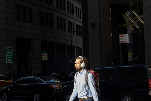 New York, NY, USA - July 7, 2022: A man wearing a headset walks on the streets in the Financial District of Manhattan in New York City, after work.