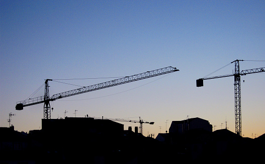 Three construction cranes back lit at dusk. Urban skyline. Lugo city, Galicia, Spain.