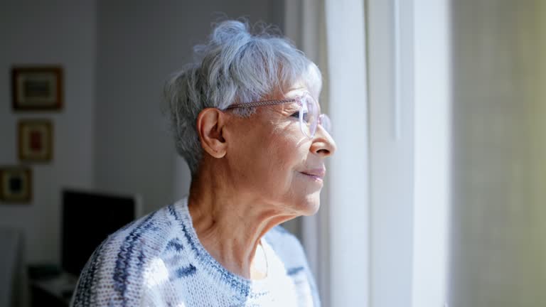 Senior woman looking out the windows of her home