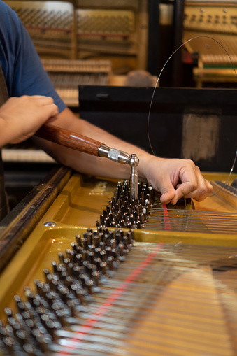 luthier repairing piano, hands making change of piano strings