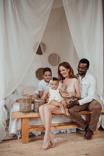 Mixed race family with white son and infant swarthy daughter spend time together at cozy apartment. African american man with his fair skinned wife kids enjoy togetherness positive emotion at home
