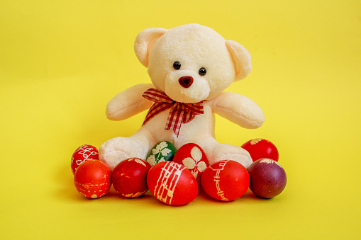 Teddy bear surrounded with colourful Easter eggs on a yellow background