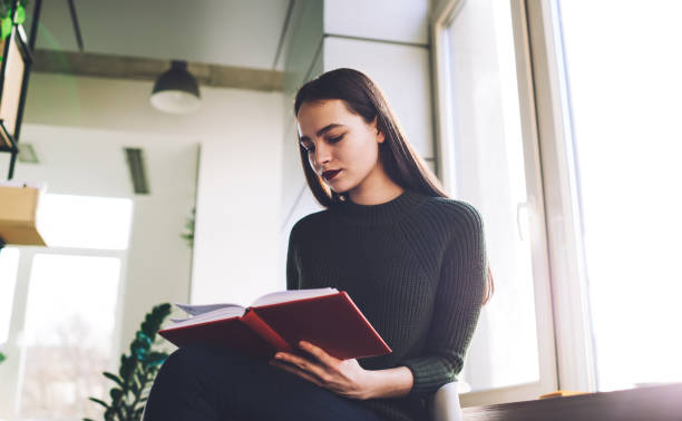 istock Young woman reading book in cozy room 1473304537