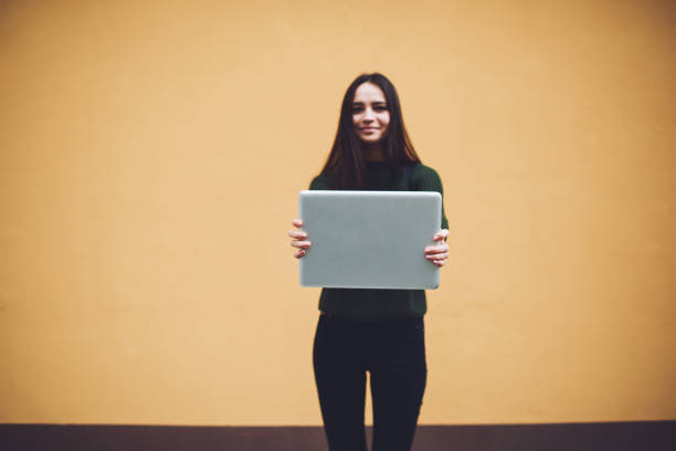 istock Female showing laptop while standing near wall 1473304621