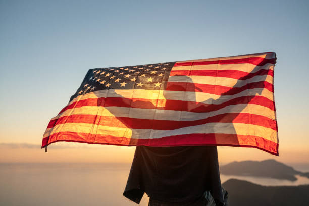 pria yang bangga mengibarkan bendera amerika serikat berdiri di puncak gunung saat matahari terbenam - america flag potret stok, foto, & gambar bebas royalti