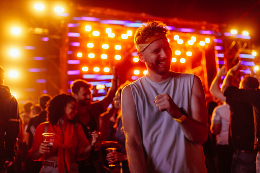 A young adult ginger Caucasian man is dancing at a music concert in open air.