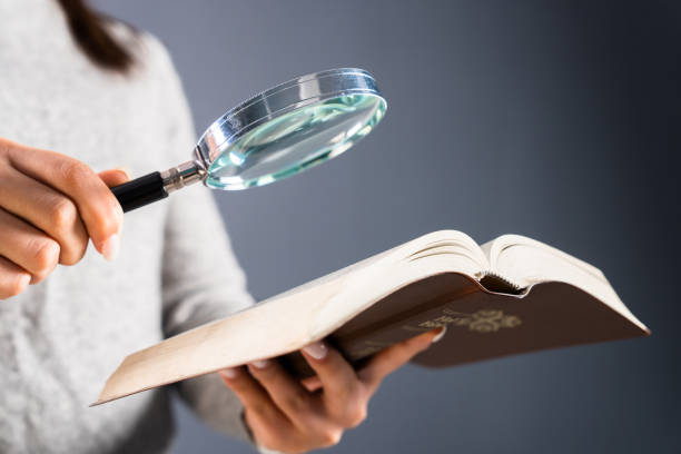 istock Woman looking at a book with a magnifying glass 1473307548