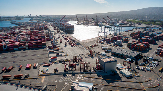 Container transportation is now the most popular way of cargo movement and a critical pillar of the global economy, Shipping Containers in Stacks in Port of Long Beach During the Day with Light Clouds Overhead
