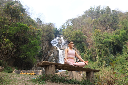 , Healthy woman exercise Yoga  at front of waterfall in green forest . Serenity and yoga practicing at waterfall , MaeTia waterfall located in Chiangmai of Thailand .