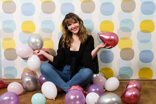 Young Woman Sitting and Holding Balloons in Hand Against Colorful Background