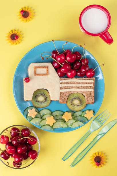 Healthy toast for kids in shape of car with cherry, kiwi, cucumber and cheese on blue plate on yellow background, top view stock photo