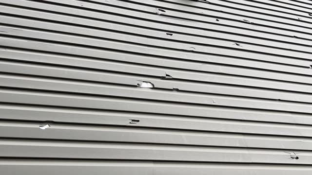 Holes in the exterior siding of the home from hail storm damage.