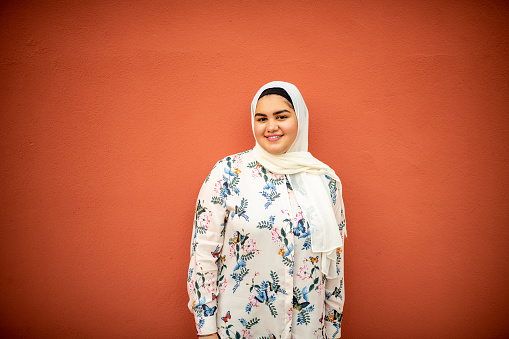 Portrait of a smiling Muslim looking at the camera. She is leaning on a red background