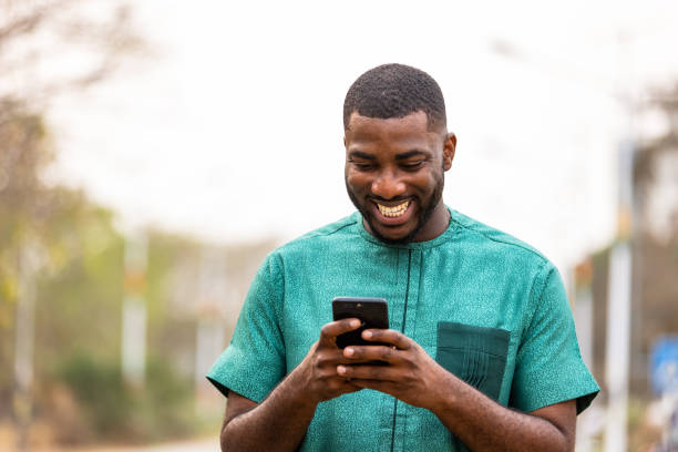 Young African Man Mobile banking on-the-go with smartphone. Young African Man Mobile banking on-the-go with smartphone, Portrait of Ghanaian man holding cellphone west africa stock pictures, royalty-free photos & images