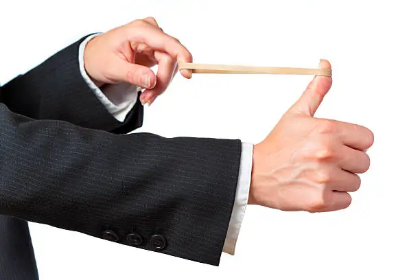 Hands stretching a rubber band as to shoot it. Person dressed in business attire and isolated on white. Focus on thumb.