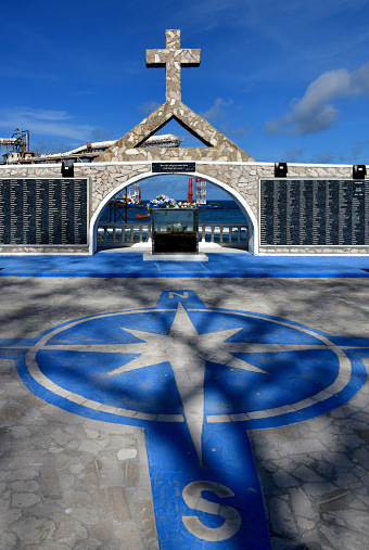 Orro, Aiwo District, Nauru: World War II Memorial Monument, pays homage to the Nauruans that perished on Truk / Chuuk and Nauru - wall with names with cross and triangle forming the alchemical symbol of phosphorus, pavement with compass rose - harbor cantilevers in the background.