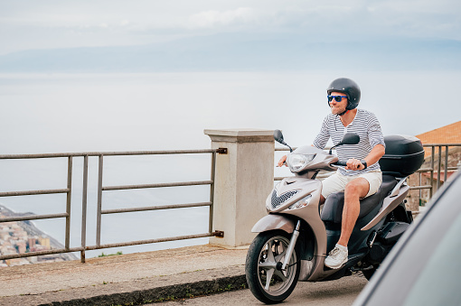 Hombre alegremente sonriente con casco y gafas de sol montando rápidamente el moto scooter en las calles del casco antiguo siciliano en forza d'Agro. Feliz concepto de vacaciones y transporte italiano. photo
