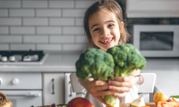istock Funny little girl with broccoli in the kitchen. 1473332033