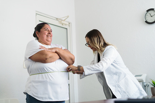 A female nutritionist measuring the waist of an overweight latin woman.