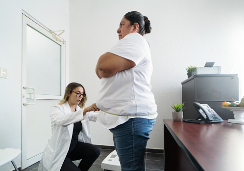 A female nutritionist measuring the hip of an overweight latin woman.