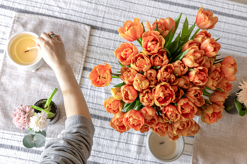 Orange tulips, candle and other spring flowers on the table, serving and decor concept, cozy home, top view.