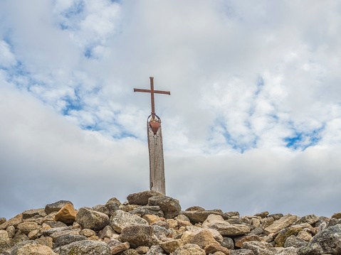 An imposing stone cross emerges majestically in the middle of a vast field of rapeseed in full bloom. The intense yellow of the flowers creates a captivating contrast with the clear, uncluttered blue of the rural sky. The cross, with its antiquity engraved in every crevice, seems to hold silent history as the rapeseed waves gently in the wind, weaving a landscape that evokes the tranquility and serenity of country life.