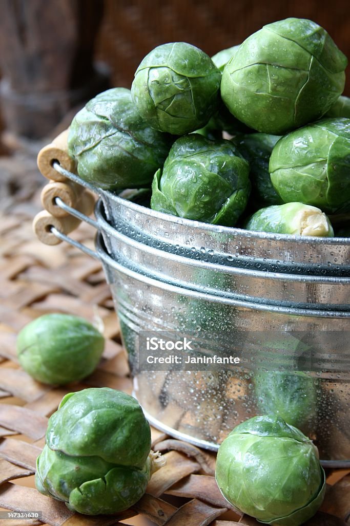 Close-up of a basin overflowing with Brussels sprouts A bunch of brussels sprouts in a stack of small tin buckets. Three brussels sprouts laying outside the bucket on a leather surface. Brussels Sprout Stock Photo