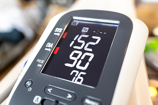 Close up of a digital home blood pressure monitor showing high diastolic and systolic numbers, representing an unhealthy lifestyle and possible hypertension.