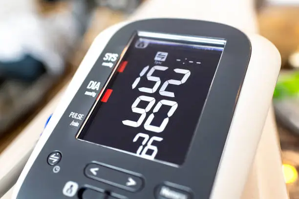 Photo of Close up of a digital home blood pressure monitor showing high diastolic and systolic numbers, representing an unhealthy lifestyle and possible hypertension.