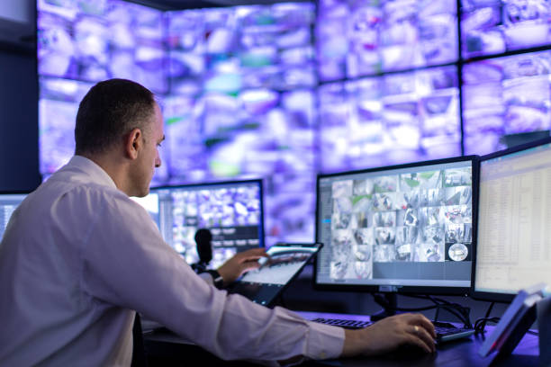 homme travaillant dans une salle de surveillance et regardant des moniteurs - salle de contrôle photos et images de collection