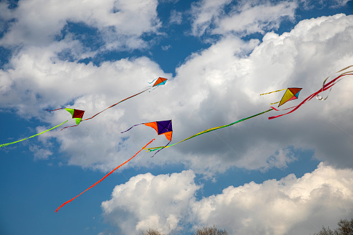 Kites flying in blue and cloudy sky, kite festival. Colorful kites flying among the clouds with the spring winds