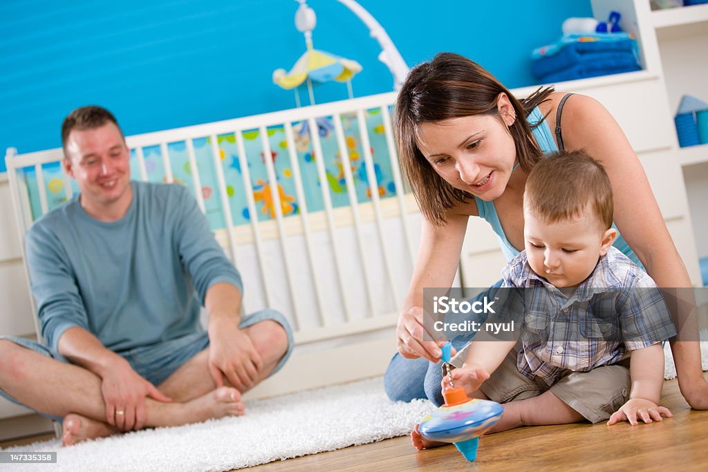 Happy family playing at home Portrait of happy family at home. Baby boy ( 1 year old ) and young parents father and mother sitting on floor and playing together at children's room, smiling. Click here for more baby photos: 30-39 Years Stock Photo