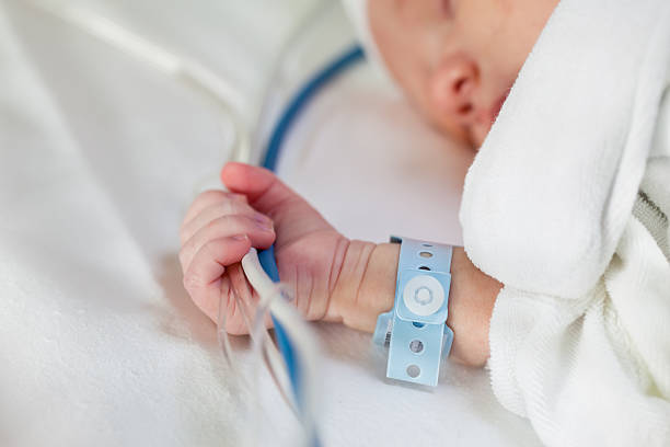 Newborn baby hanging on for life Close-up of a caucasian newborn baby holding life-support hoses and cables tight in his had with wrist nametag while sleeping in a hospital bed. babies only stock pictures, royalty-free photos & images