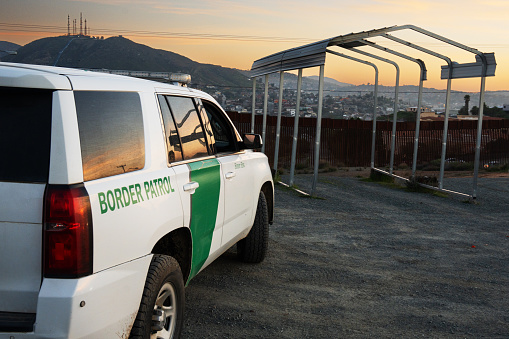 United States Border Patrol Vehicle Parked Along International Border Barrier Between Mexico and US Near Tecate Tijuana at Dusk Conducting Surveillance Against Illegal Immigration