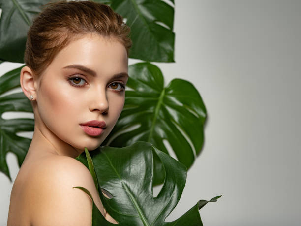 Beautiful woman with green leave near face and body. Closeup girl's face with green leave. Pretty girl in Skin care beauty treatments concept. Model with big tropical leaf, posing, studio. Brown makeup. hermosa mujer con hojas verdes cerca de la cara y el cuerpo. primer plano de la cara de la niña con hoja verde. pretty girl en el concepto de tratamientos de belleza para el cuidado de la piel. modelo con gran hoja tropical, posando, estudio. maquillaje m