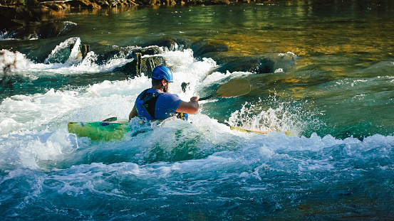 Caucasian man kayaking upstream on the whitewater rapids, paddling hard on the turbulent river