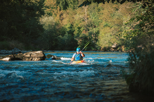 Caucasian man skillfully steering kayak in the river, crossing over whitewater rapids