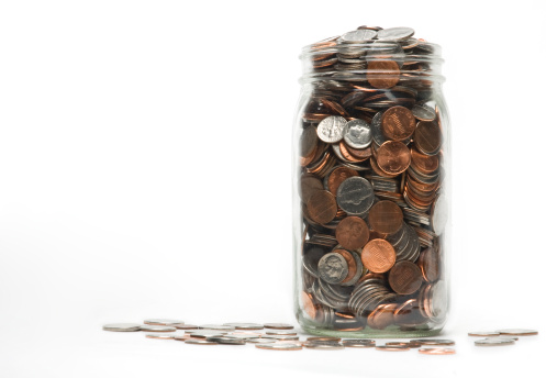 Image of a jar of change with some spilling over onto the surface below.