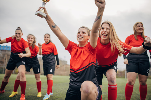 Group of women, happy female rugby team players on celebrating on a rugby field outdoors together, they won a trophy.