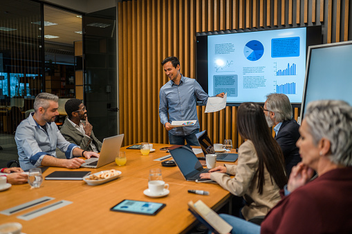 Asian mid adult CEO holding a business meeting. Standing in a modern board room updating business colleagues with results on past activities and future plans.