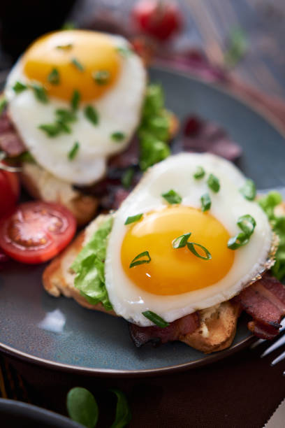 istock Tasty breakfast - fried egg toasts, bacon, tomatoes on wooden kitchen table 1473377761